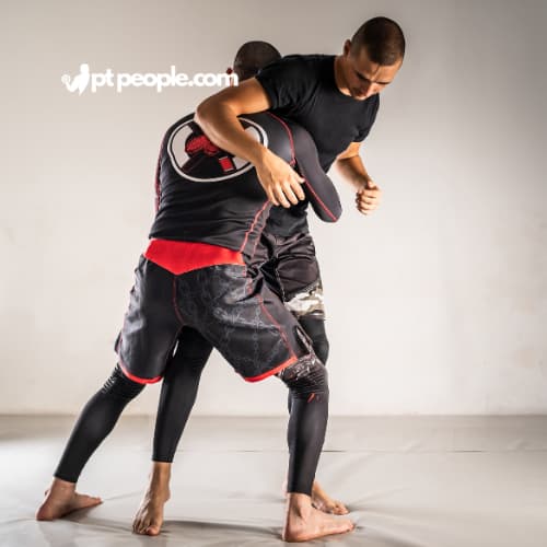 Two determined individuals in the UAE grapple on the mats during an MMA training session overseen by a professional MMA coach. They showcase a mix of striking and grappling techniques.